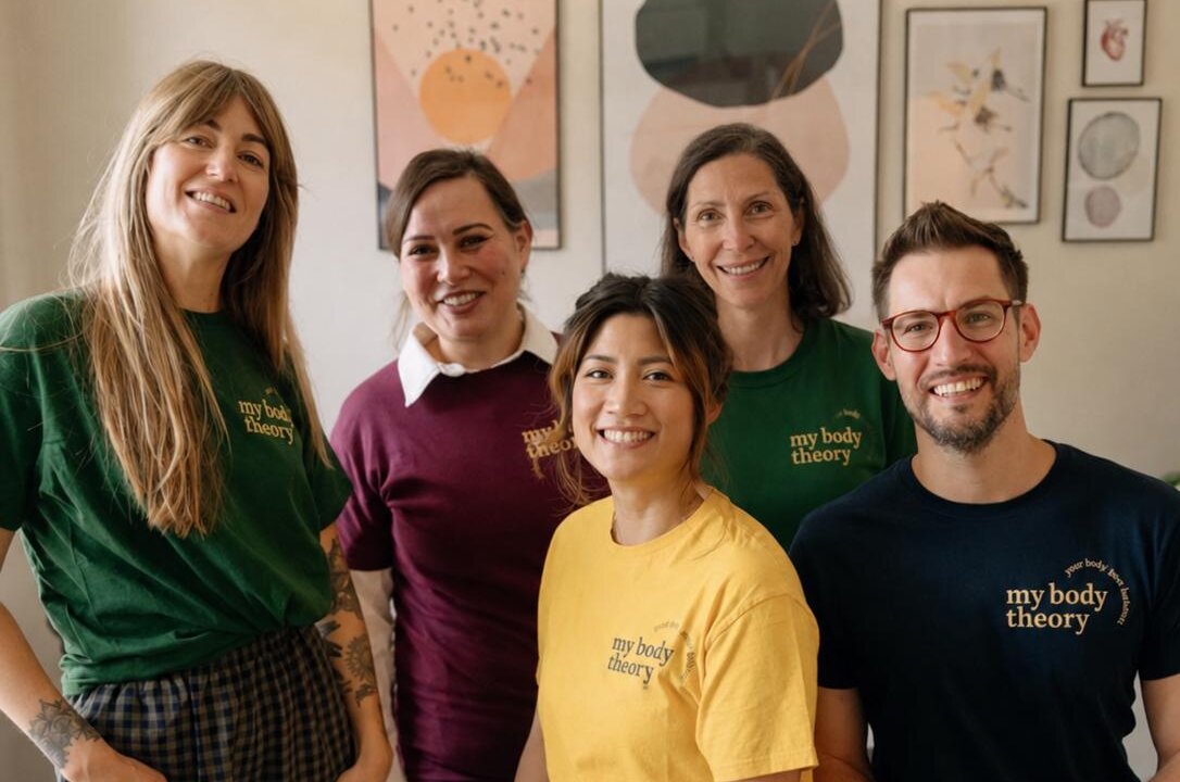 Das Team von MyBodyTheory vor der Bilderwand in der Praxis