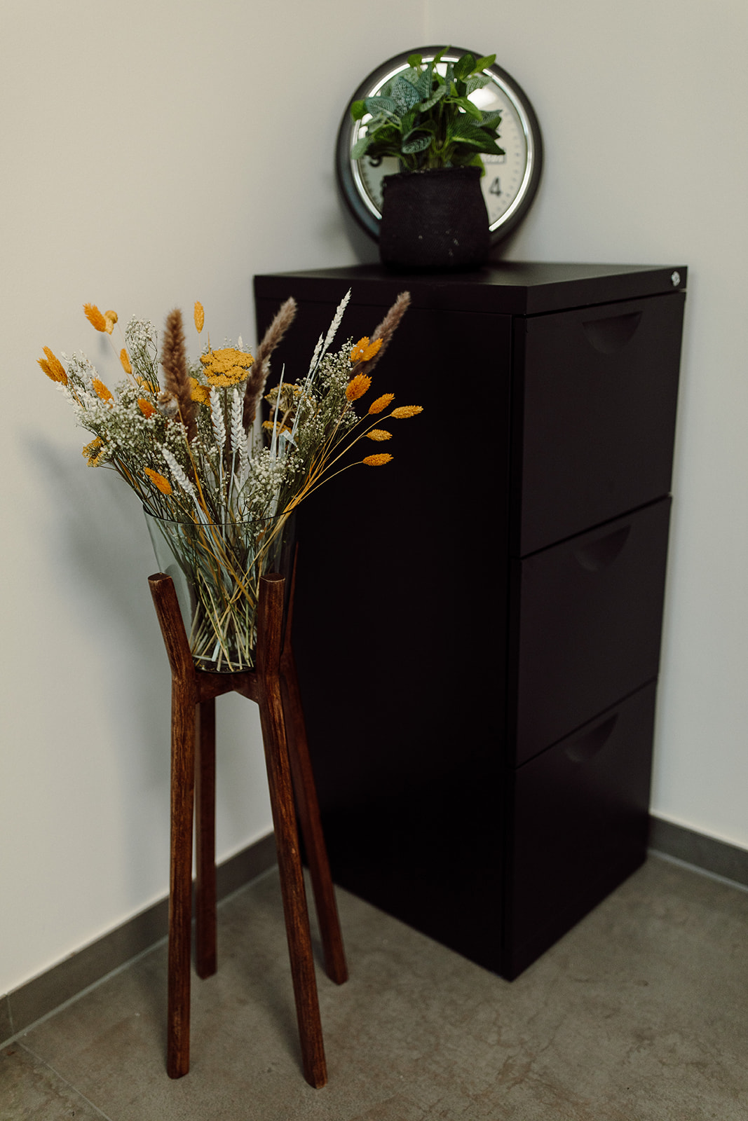 Schwarzer Schrank mit Trockenblumen und rundem Spiegel